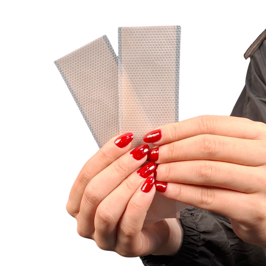 Manos femeninas manipulando una lámina de silicona adhesiva color piel sobre una base texturizada, ideal para el tratamiento y camuflaje de cicatrices.