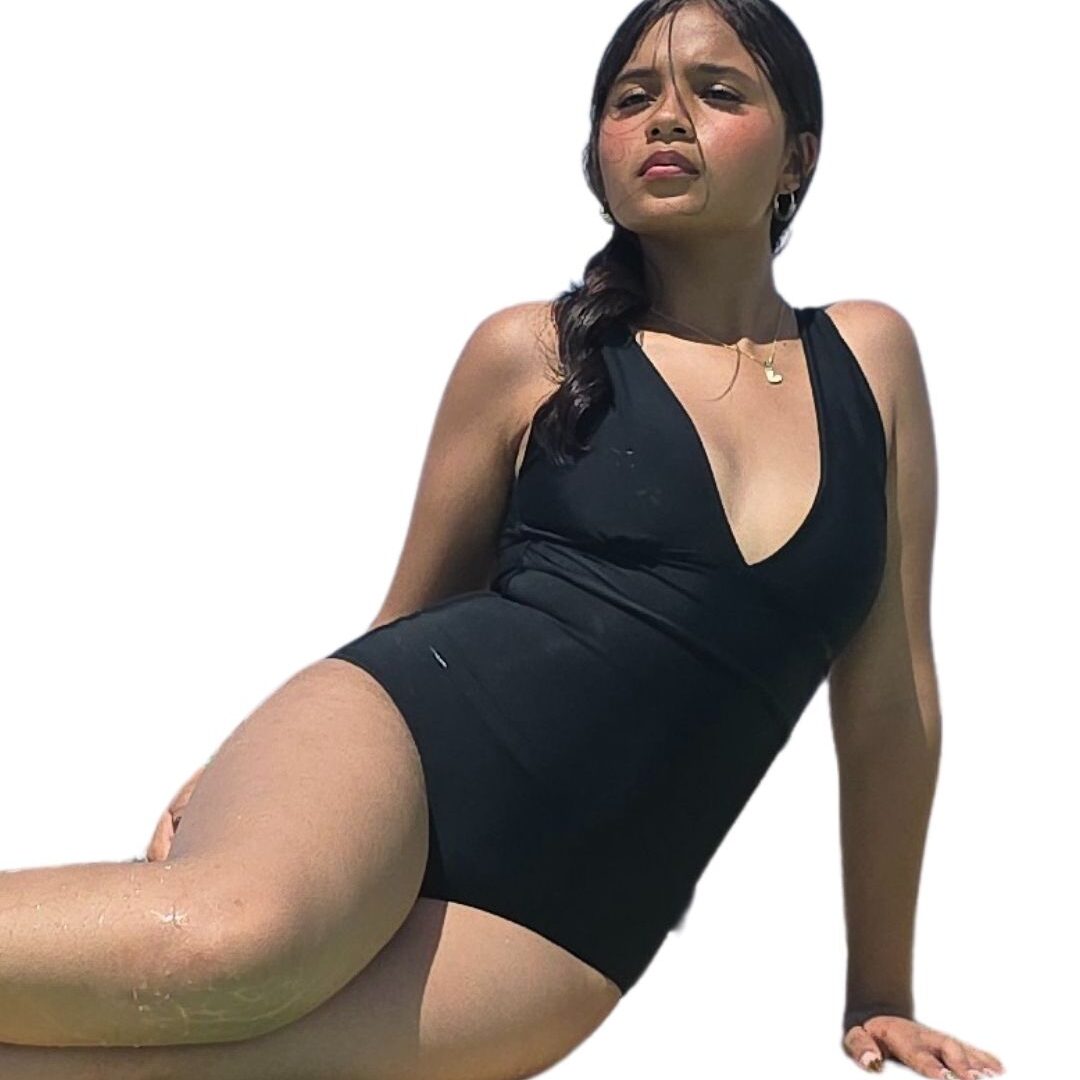 Mujer modelando un elegante traje de baño entero negro, con un profundo escote en V al frente y un detalle de lazo anudado en la espalda baja, equipado con una faja interna de alta compresión.