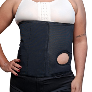 Persona usando una banda abdominal elástica de color negro diseñada para colostomía, con una apertura circular reforzada en el lateral izquierdo para la bolsa de estoma y cierre de velcro frontal.