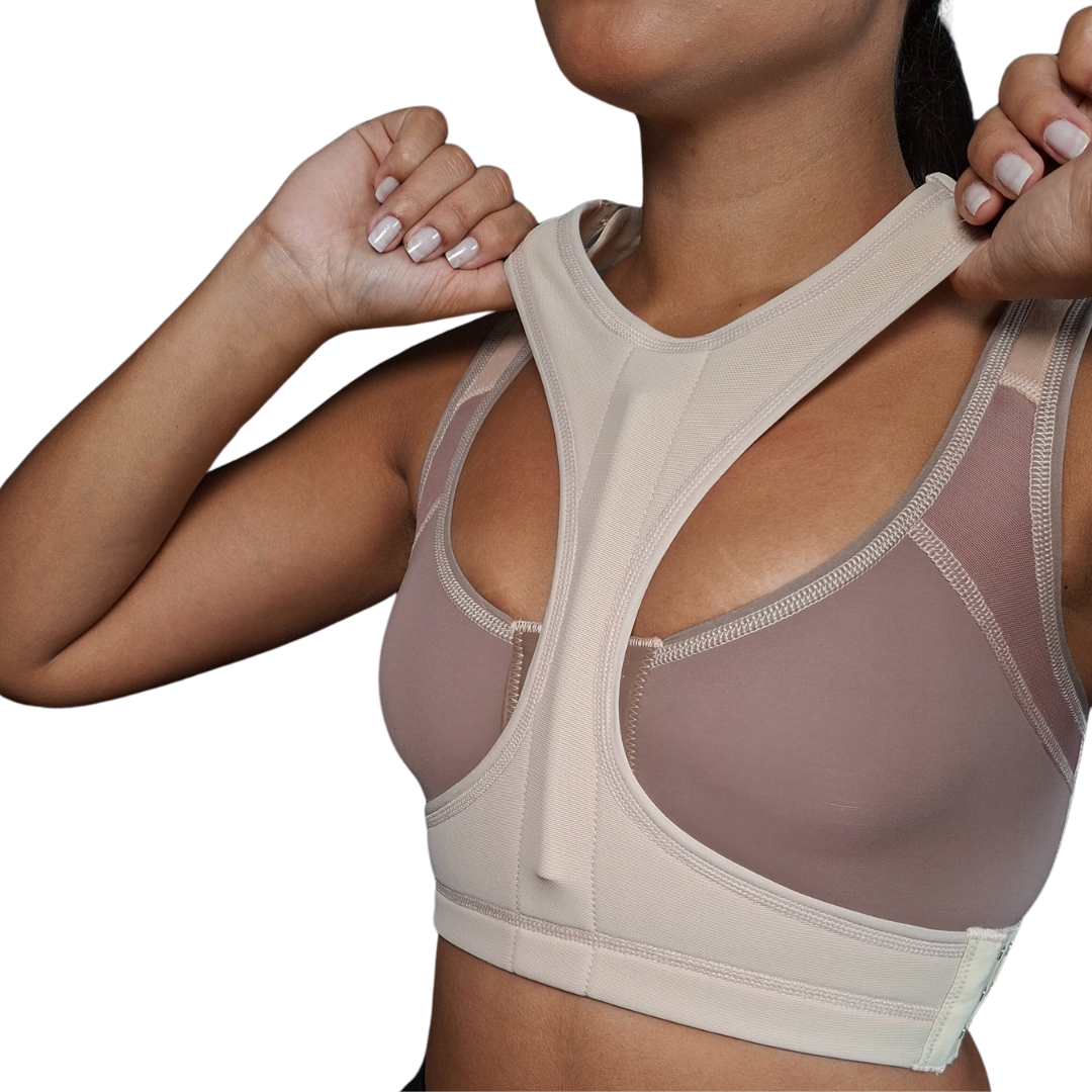Mujer modelando un separador de senos postquirúrgico de color beige, con un diseño anatómico en forma de "T" que se ajusta entre los bustos para mantener la separación natural después de una cirugía de implantes.