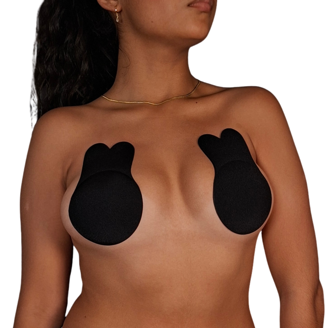 Vista de perfil de una mujer utilizando pezoneras adhesivas de color negro con diseño anatómico en forma de orejas de conejo, adheridas directamente sobre el busto para proporcionar elevación e invisibilidad total.