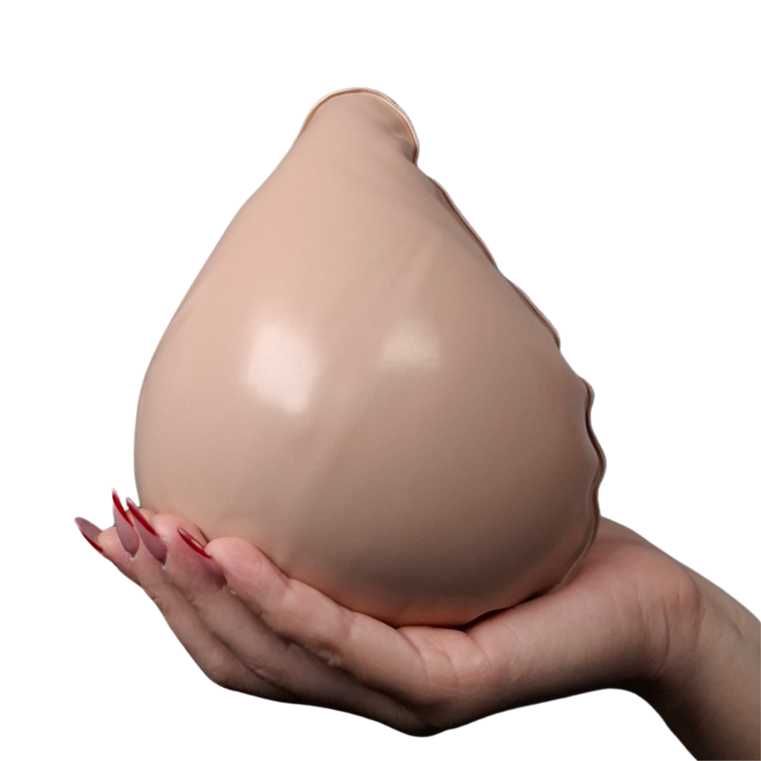 Manos sosteniendo dos prótesis mamarias externas de color piel, una totalmente inflada con forma anatómica y otra desinflada para mostrar su flexibilidad.