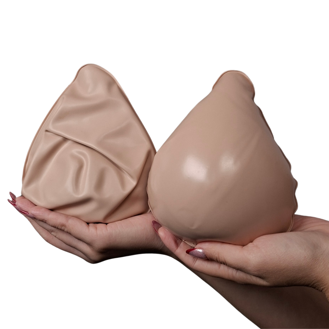 Manos sosteniendo dos prótesis mamarias externas de color piel, una totalmente inflada con forma anatómica y otra desinflada para mostrar su flexibilidad.