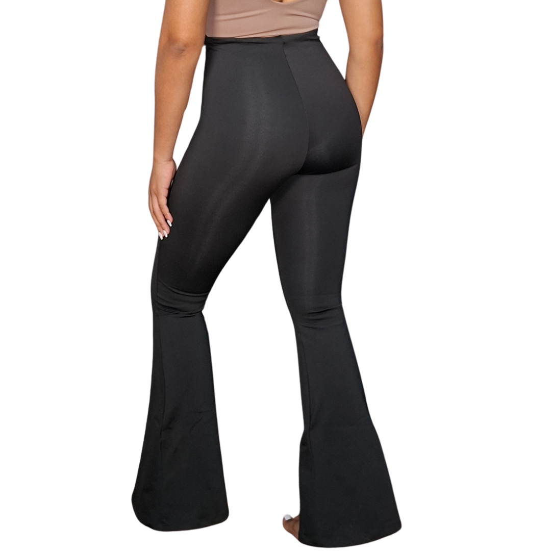 Mujer luciendo un pantalón negro de vestir estilo bota campana, combinado con una faja interna integrada de alta compresión que moldea el abdomen y define la cintura.