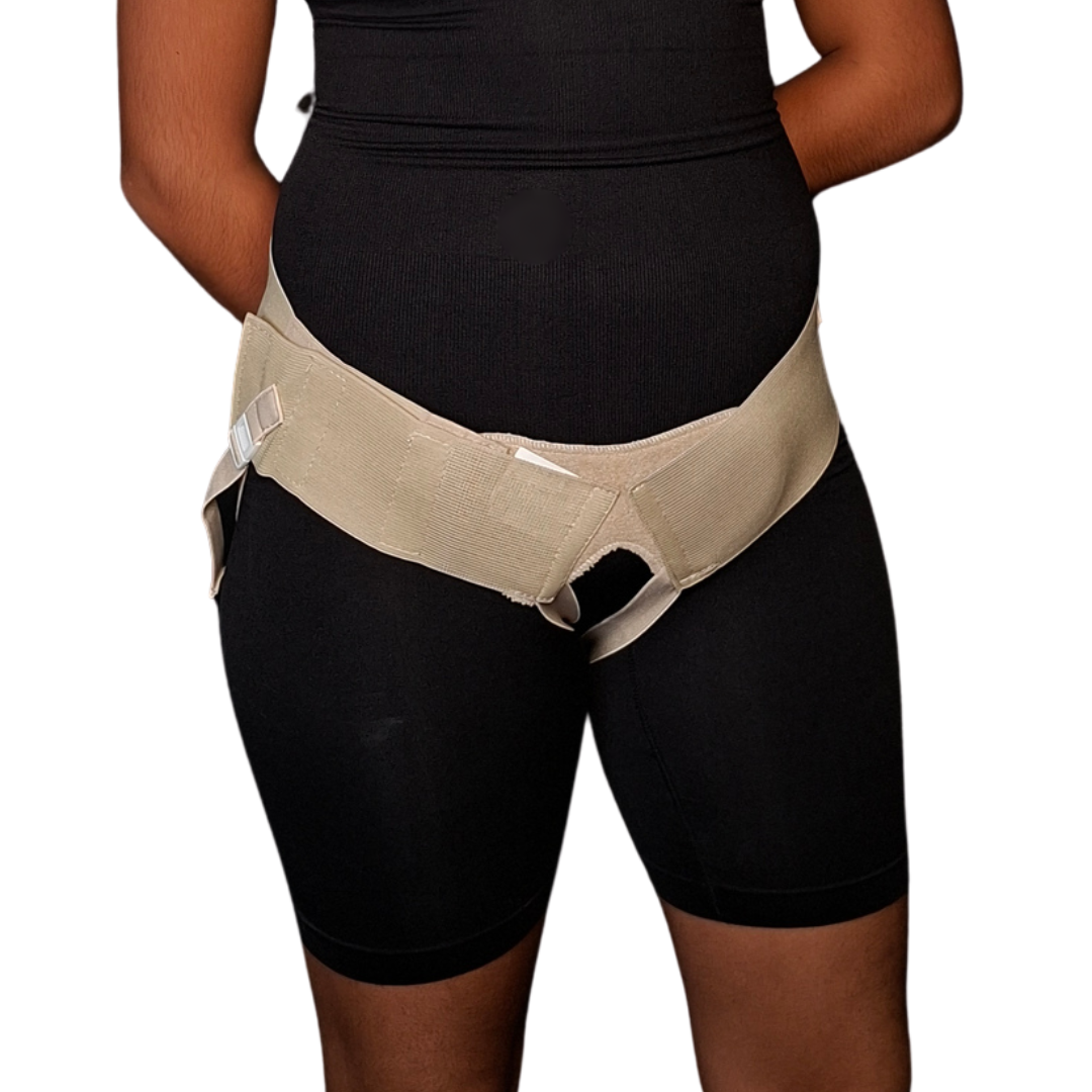 Vista frontal y posterior de un braguero inguinal unisex en tono beige o crema colocado sobre prenda ajustada negra. Muestra una banda pélvica elástica ancha con sistema de ajuste mediante broche plástico y correas perineales ajustables que pasan por debajo de la zona glútea para brindar compresión localizada en la región inguinal.
